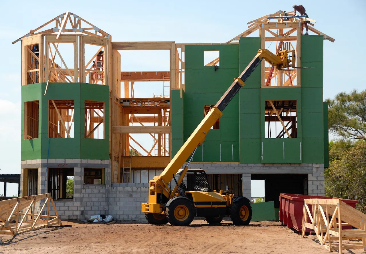A yellow and black heavy equipment near an unfinished building.