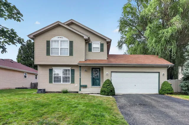Front exterior of a two-story home with tan siding, green shutters, and an attached two-car garage, coming soon in Pheasant Landing, Plainfield