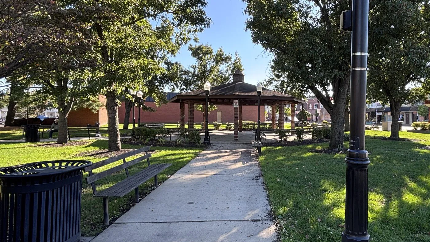 Brick gazebo and benches in a shady park in Maple Shade, NJ, with Main Street shops in the background