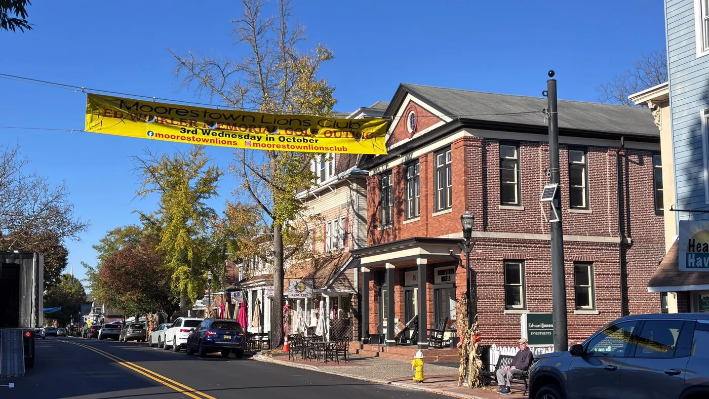 Main Street in Moorestown, NJ with brick storefronts, fall trees and a Moorestown Lions Club banner overhead