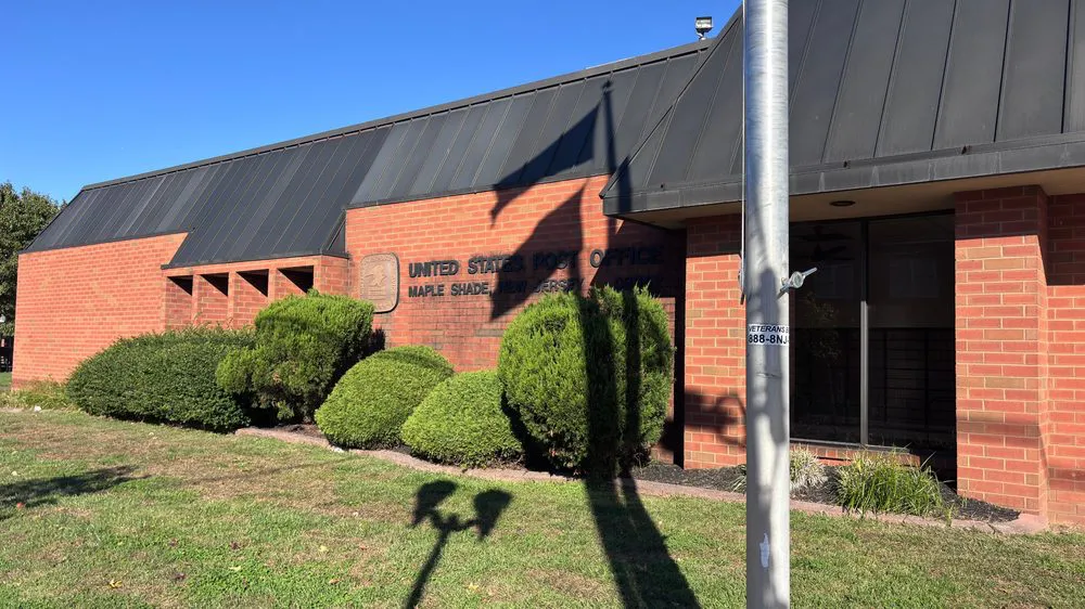 Maple Shade, New Jersey post office, a red brick building with a dark metal roof and shrubs out front