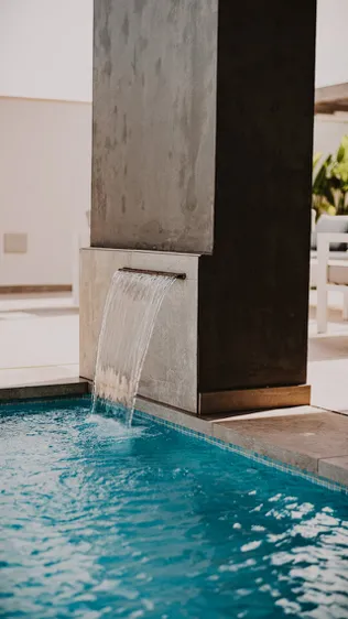 A small waterfall coming out of a column into a swimming pool