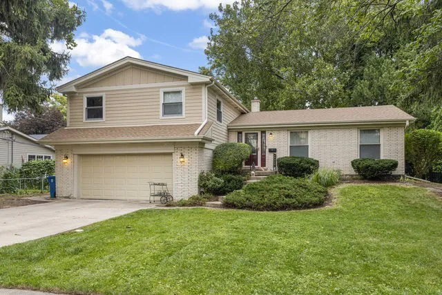 Front exterior of a tri-level split-level with tan siding, cream brick, red front door, and two-car garage, coming soon in Downers Grove